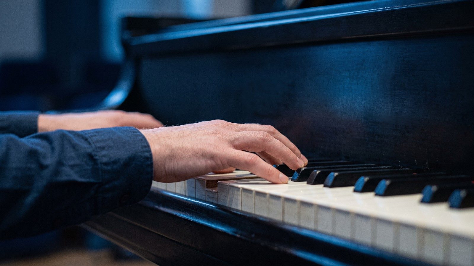 Gros plan sur les mains d'un pianiste jouant un accord de trois notes sur les touches d'un piano, dans une lumière bleue douce